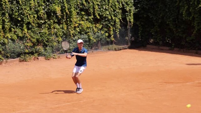 Male tennis player reaching low forehand shot on clay tennis court. Concept of athletic effort, competitive tennis, flexibility, fast reactions, sports performance and outdoor training.