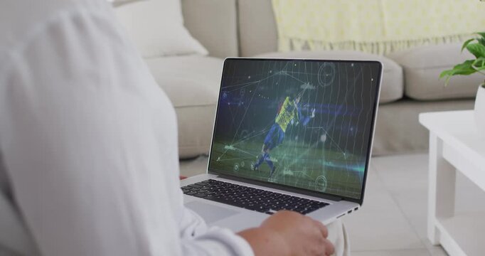 Female viewer at home with laptop on lap playing soccer match, watching attacker shooting for goal