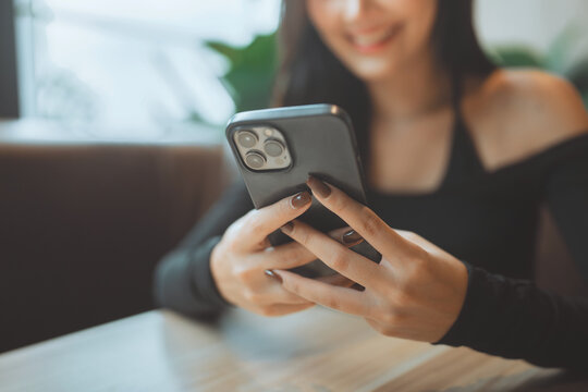 Close up of happy Asian woman typing text message on smartphone while sitting at cafe, smiling female using mobile phone for online shopping, chatting, or mobile banking for modern digital lifestyle, 