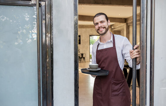Startup successful sme small business local owner caucasian man barista wear apron stand at the modern coffee shop, welcome customers hospitality, and customer service.