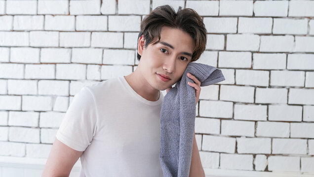 Portrait of a smile asian man with towel on shoulders looking at camera. Happy young man relax after training. Moving routine bathroom or sporty active guy resting after workout with copy space.