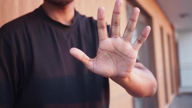Close up shot of person holding hand up in stop gesture, outdoors against building background