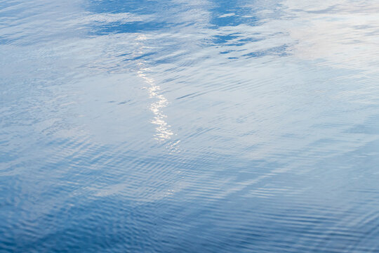 Shiny blue still water surface with smooth ripples and bright reflections, abstract natural background photo texture
