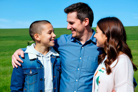 Caucasian father embracing teenage son and daughter, smiling and bonding outdoors in family support concept. Useful for parenting, family values, insurance, healthcare campaigns