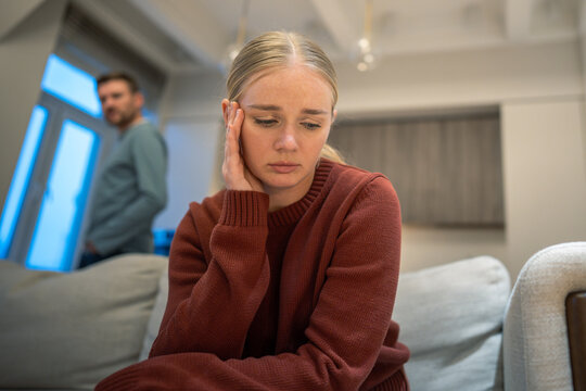 Woman sitting on couch feeling unhappy and sad after emotional domestic quarrel with man partner, mental pressure, manipulations and disappointment in couple relationships, breakup and apathy.