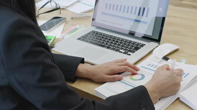 Close-up of businesswoman hands writing on documents while using computer