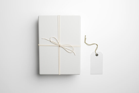 White gift box mockup wrapped in textured paper with string bow, vertical top view blank hang tag template detached on side of cardboard parcel package isolated on white background, 3d render