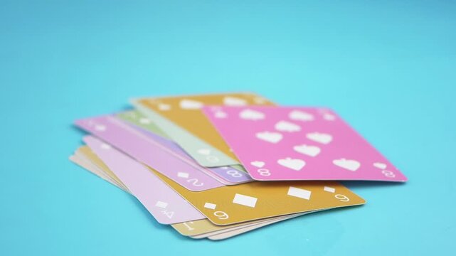 Colorful playing cards falling onto a pile against light blue background in slow motion cinematic video
