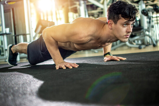 Shirtless athletic young man doing intense pushups on a mat at gym