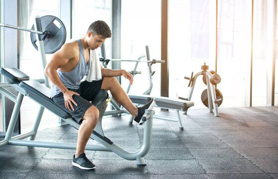 Young athletic man resting on a bench press after workout in modern gym