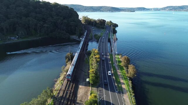 Intercity train Sydney to Newcastle. Train stop Woy Woy.Train travels alongside river with road in view during a sunny day near a forested area
