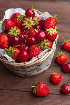 Fresh strawberries and cherries in a basket on a wooden table in a kitchen setting during the day
