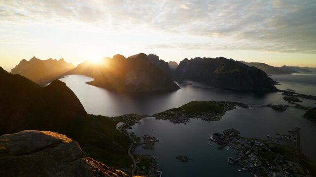 Sunrise rays break over jagged peaks as Reine village and surrounding fjords lie still below the Reinebringen viewpoint.