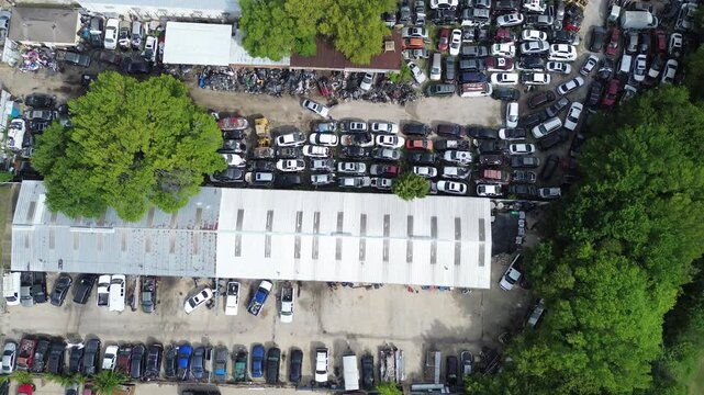 Elongated metal distribution buildings stand surrounded by trees on regional commercial plots. Closely managed scrap automobile collections maximize land in Pleasant Grove area, Dallas, Texas