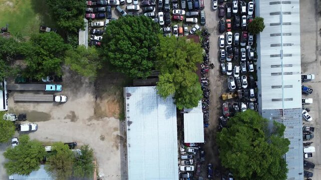 Expansive aluminum structures shield interior junkyard operations within neighborhood corridors. Clustered automotive scraps, industrial warehouse roofing maximize usable acreage in Dallas, TX