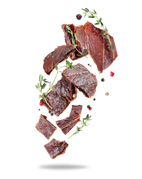 Pieces of delicious beef jerky with ingredients in the air isolated on a white background