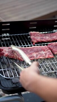 Vertical video of hand placing raw beef on a barbecue grill