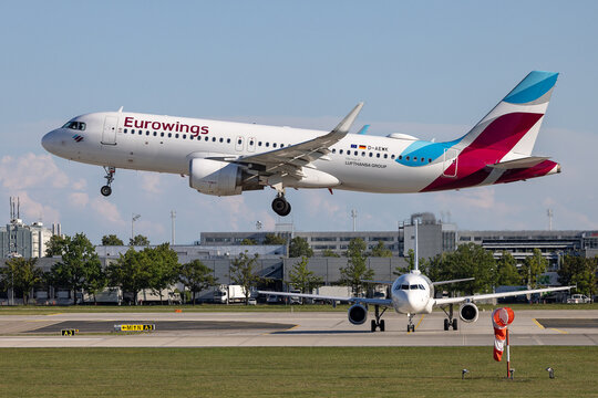 Ein Airbus A320 der Eurowings (Lufthansa Group) mit der Kennung D-AEWK im Landeanflug. Im Vordergrund wartet ein weiteres Schmalrumpfflugzeug auf dem Rollweg.