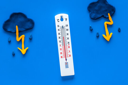 Rainy weather. Thermometer near clouds and drops on blue background top view
