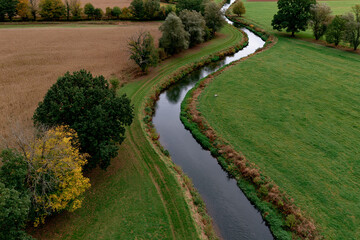 Fototapeta premium River flows through rural fields and trees