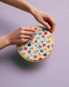 Woman embroidering colorful flowers on canvas using needle and thread in wooden hoop. Handcraft hobby as creative activity. Textile art design for home decor or DIY craft project.