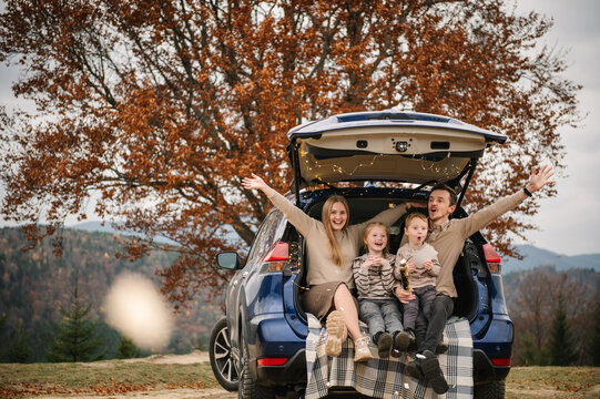 A joyful family celebrates in a car trunk, revealing news of a third baby to their children. An emotional moment with confetti during a cozy autumn picnic in the mountains.