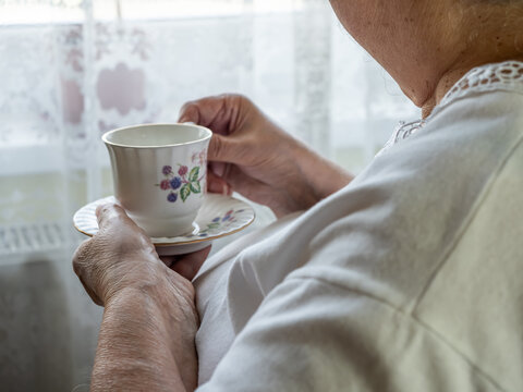 Close Up of Senior Woman Holding Floral Tea Cup Near Bright Window