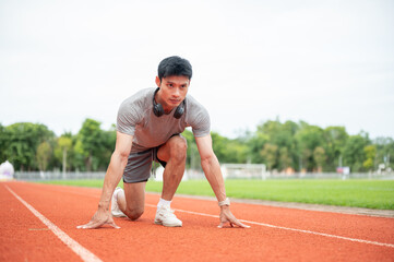 Fototapeta premium Asian man sprinter focused while crouching in start position ready to run on track in sports stadium