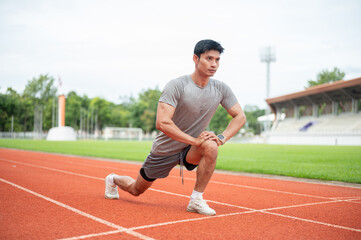 Fototapeta premium Asian male runner stretching legs in side lunge position on running track in sports stadium.
