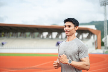 Fototapeta premium Asian athletic man running happily with a smile on track during a workout session in sports stadium.