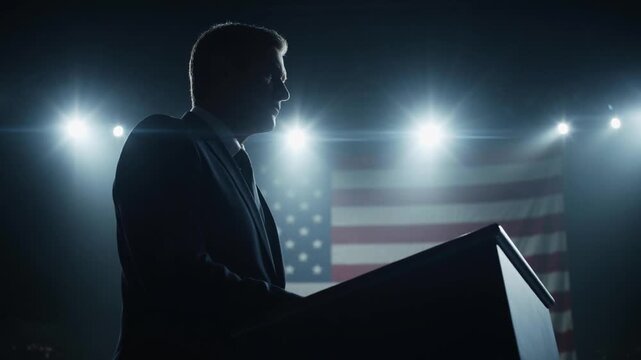 Silhouette of a politician giving a speech at a podium with the American flag and dramatic stage lights