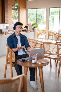 Asian freelancer man speaking during online meeting with laptop in modern cafe.