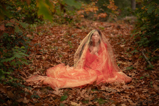 girl in red dress covered by thin fabric in autumn forest and foliage