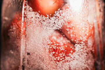 Fototapeta premium Macro view of coarse sugar crystals and condensation clinging to a glass jar, with red strawberry preserves softly visible behind.