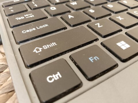 Close up perspective of a modern black laptop keyboard focusing on the shift control and function keys showing clear white lettering on dark matte square buttons for professional computing with office
