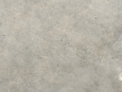 A high angle close up view of a rough grey concrete floor surface featuring a mottled texture with scattered dust particles and small debris creating a minimalist industrial aesthetic for modern
