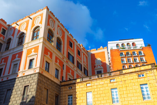Palazzo Cellammare architecture under blue sky in Naples, Italy. Historic building showcases a vibrant orange and yellow facade paired with classic rusticated stone buildings