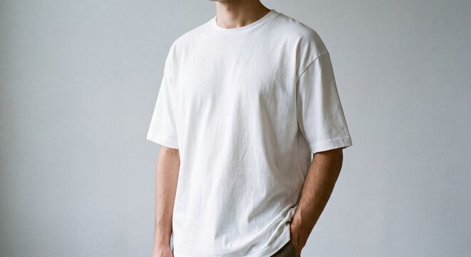 Young man wearing a blank white oversized t-shirt mockup, standing against a neutral grey wall for apparel branding