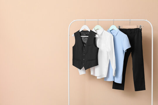 Childrens school uniform clothes including a black vest, white shirt, blue polo, and black trousers on a rack