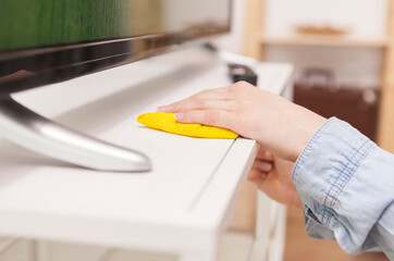 Housewife cleans dust from a TV stand in the living room, showing household cleaning, furniture...