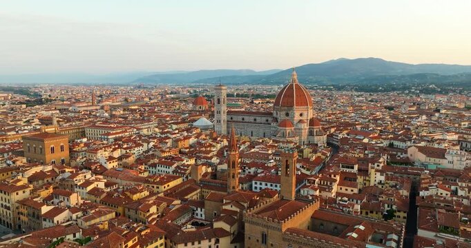 Santa Maria del Fiore cathedral Brunelleschi dome rising above historic red rooftops Florence Italy high angle aerial view dawn warm sunlight iconic Renaissance architecture travel concept.