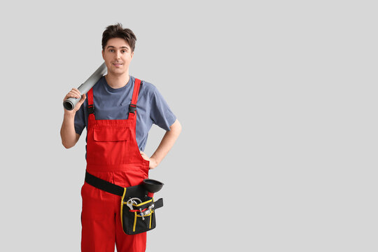 Male plumber with pipe and tool belt on grey background
