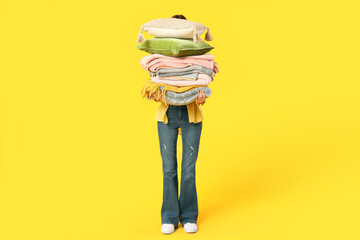 Naklejka premium Beautiful young woman with stack of different blankets and pillows on yellow background
