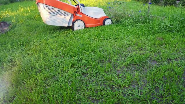 A close-up view of an orange and white lawnmower actively mowing a lush green lawn on a bright sunny day