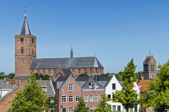 Naarden Vesting, Netherlands. Picturesque view of classic brick-facade residential houses with the grand Grote Kerk and another historic tower rising behind them.