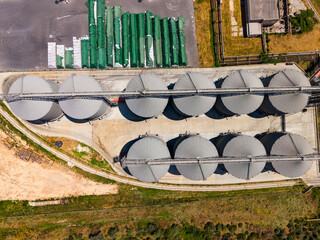Large storage silos lined up on concrete, seen from above near a green agricultural area during daytime © DSMT