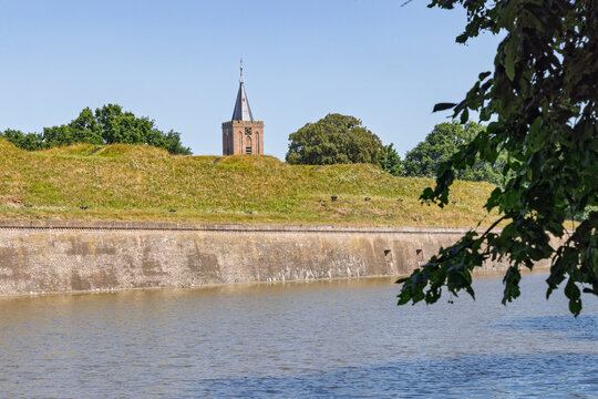 Naarden Vesting, Netherlands. The historic steeple of the Grote Kerk church peeking over the top of the monumental brick fortress wall and moat on a sunny day.