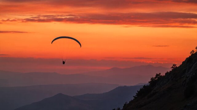 Paraglider flying over mountains at sunset