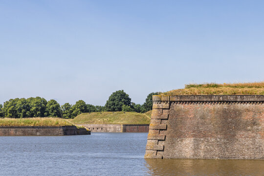 Naarden Vesting, Netherlands. Close-up view of the massive brick defensive walls of a bastion rising from the water moat under a clear blue summer sky.