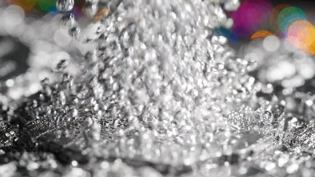 Close-up sequence of water droplets forming and merging on a metallic surface, showcasing intricate details and reflections with colorful bokeh in the background